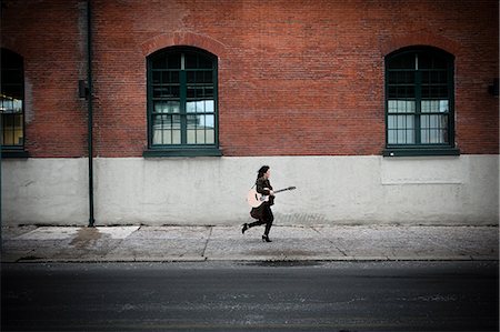 Young woman running on city sidewalk with acoustic guitar Stock Photo - Premium Royalty-Free, Code: 614-08885024