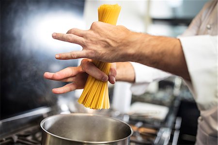 Chef putting spaghetti in saucepan on stove, close-up, overhead view Stock Photo - Premium Royalty-Free, Code: 614-08885076