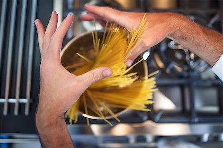 Chef putting spaghetti in saucepan on stove, close-up, overhead view Stock Photo - Premium Royalty-Free, Code: 614-08885077