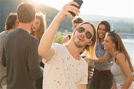 simsearch:614-08881018,k - Young man taking selfie at waterfront roof terrace party, Budapest, Hungary Fotografie stock - Premium Royalty-Free, Codice: 614-08880991