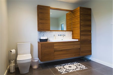 White high-back flush toilet and American walnut wood vanity with rectangular sink and ceramic tile flooring, Quebec, Canada Stock Photo - Premium Royalty-Free, Code: 614-08881126