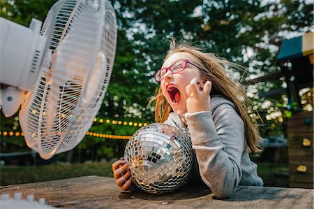 Girl screaming in front of windy electric fan at garden table Photographie de stock - Premium Libres de Droits, Code: 614-08881314