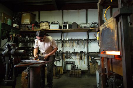 Male metalsmith hammering metal on workshop anvil Stock Photo - Premium Royalty-Free, Code: 614-08881416