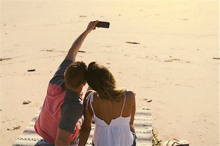 Rear view of couple sitting on beach taking smartphone selfie, Newport Beach, California, USA Stock Photo - Premium Royalty-Free, Code: 614-08881423