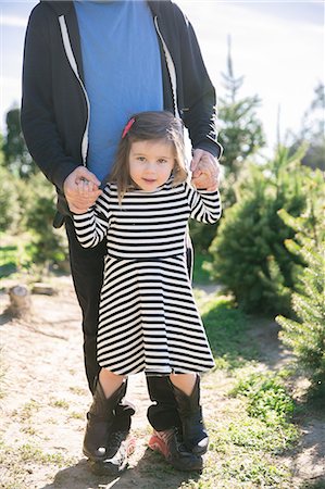 Portrait of small girl holding father's hands and standing on his feet by fir trees Stock Photo - Premium Royalty-Free, Code: 614-08908275