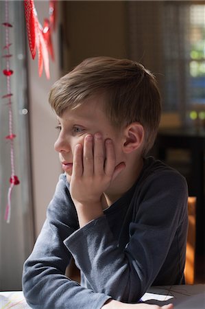 soñar despierto - Boy sitting at table with chin on hand, gazing Foto de stock - Sin royalties Premium, Código: 614-08908316