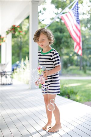 Boy making bubbles from toy bubble maker on porch Photographie de stock - Premium Libres de Droits, Code: 614-08908406