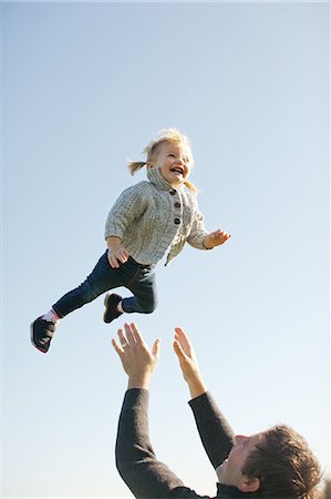 father throwing child - Female toddler thrown mid air by father against blue sky Stock Photo - Premium Royalty-Free, Code: 614-08926030