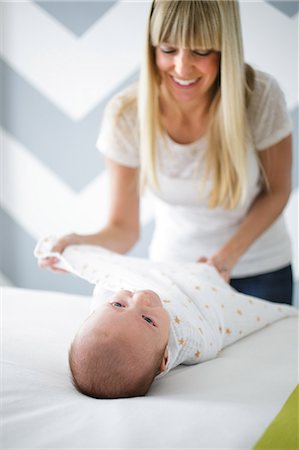 Mid adult woman swaddling baby son on bed Stock Photo - Premium Royalty-Free, Code: 614-08926073