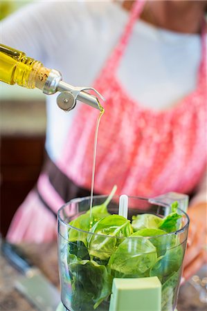 Mature woman pouring olive oil into food processor containing basil, making pesto sauce, mid section Stock Photo - Premium Royalty-Free, Code: 614-08926193