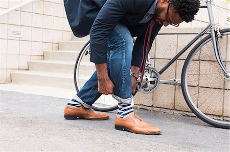 Young male cyclist rolling down jeans on railway station platform Stock Photo - Premium Royalty-Free, Code: 614-08926452