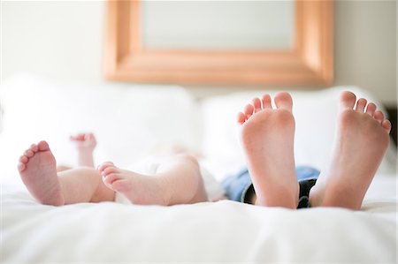 sister lying - Young girl and baby brother lying on bed, focus on feet Stock Photo - Premium Royalty-Free, Code: 614-08946145