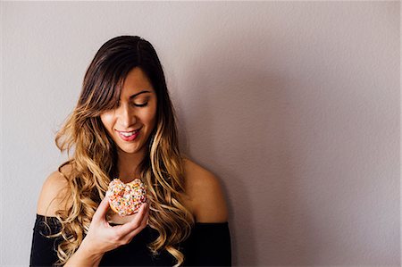 Young woman with long blond hair holding doughnut hole Stock Photo - Premium Royalty-Free, Code: 614-08946389