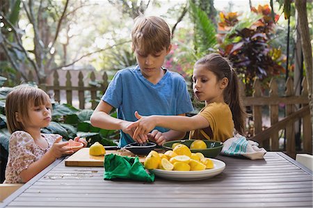 Boy and two young sisters preparing lemon juice for lemonade at garden table Stock Photo - Premium Royalty-Free, Code: 614-08946607