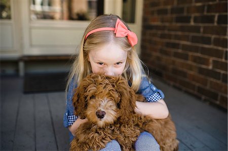 Portrait of girl kissing red haired puppy on front porch Stock Photo - Premium Royalty-Free, Code: 614-08982780