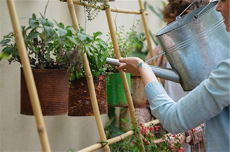 Young man and woman tending to plants growing in cans, young woman watering plants using watering can Stock Photo - Premium Royalty-Free, Code: 614-08982817