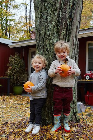 simsearch:614-08982907,k - Portrait of boy and male toddler leaning against garden tree holding pumpkins Fotografie stock - Premium Royalty-Free, Codice: 614-08982908
