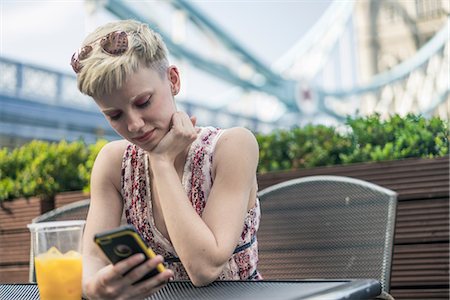 Young woman sitting outdoors, plastic drinking glass in front of her, looking at smartphone Stock Photo - Premium Royalty-Free, Code: 614-08983261