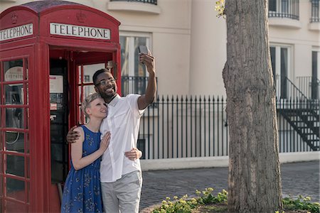 red call box - Young couple standing beside red telephone box, looking up, smiling Stock Photo - Premium Royalty-Free, Code: 614-08983283
