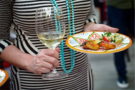 Woman holding glass of wine and plate of food, mid section Stock Photo - Premium Royalty-Free, Code: 614-08983291