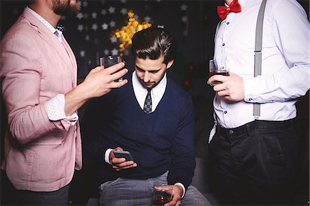 Three men at party, man in middle using smartphone Foto de stock - Sin royalties Premium, Código: 614-08983338