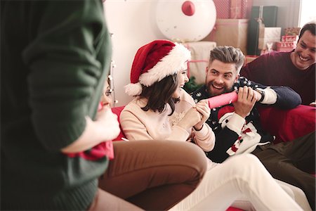 Young adult friends pulling christmas crackers on sofa at christmas party Stock Photo - Premium Royalty-Free, Code: 614-08983455