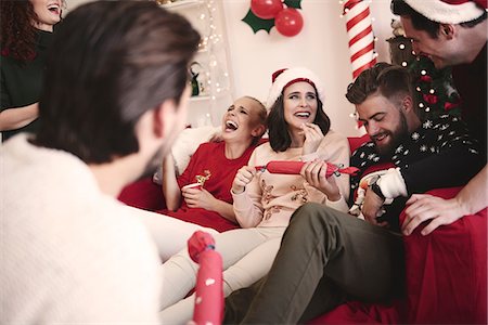 Young adult friends pulling christmas crackers on sofa at christmas party Stock Photo - Premium Royalty-Free, Code: 614-08983456