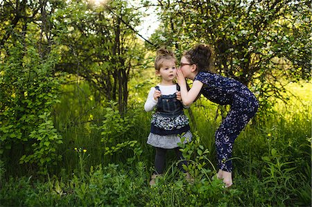 secret whisper not illustration and two people - Girl whispering to little sister in field with trees Stock Photo - Premium Royalty-Free, Code: 614-08983585