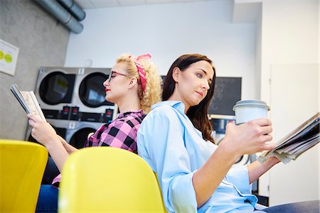 Two women reading newspapers back to back in laundrette Stock Photo - Premium Royalty-Free, Code: 614-08983607