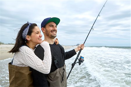 Waist down rear view of young couple in sea fishing waders on beach stock  photo