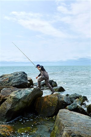 Young male sea fisher stepping over beach rocks Fotografie stock - Premium Royalty-Free, Codice: 614-08990748