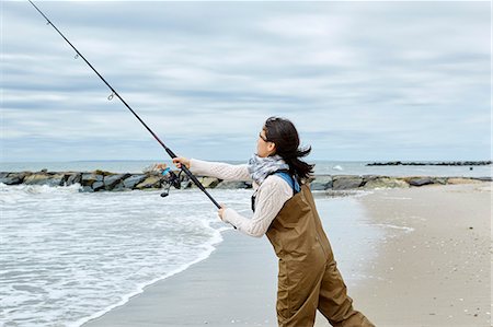 fishing pole in ocean pictures - Young woman in waders casting sea fishing rod from beach Stock Photo - Premium Royalty-Free, Code: 614-08990759