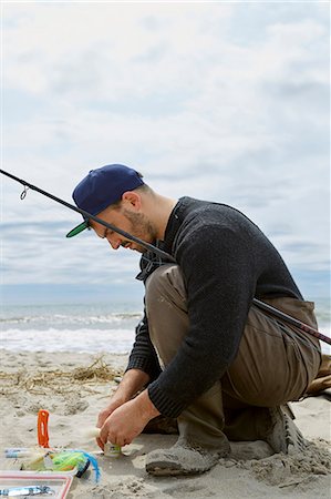 simsearch:614-09057014,k - Crouching young man preparing fishing hook on beach Fotografie stock - Premium Royalty-Free, Codice: 614-08990751