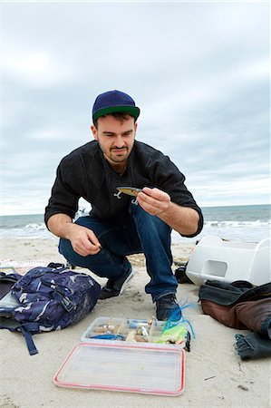 simsearch:614-09057014,k - Young male sea fisher looking at hook while crouching on beach Fotografie stock - Premium Royalty-Free, Codice: 614-08990770