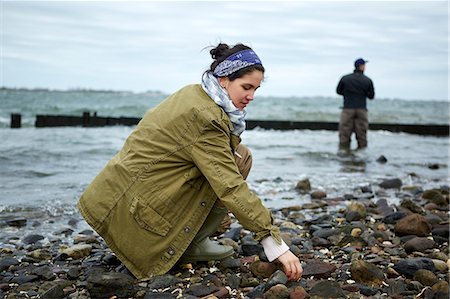 females in hip waders - Young woman crouching on beach while boyfriend sea fishing Stock Photo - Premium Royalty-Free, Code: 614-08990800