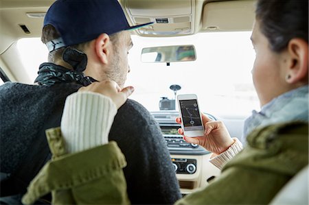 roadtrip gps - Young couple sitting in car, woman holding smartphone with map on screen, rear view Stock Photo - Premium Royalty-Free, Code: 614-08990811