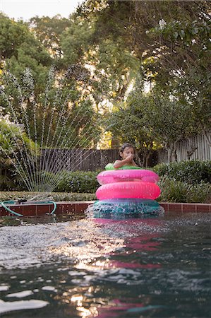 plugging nose - Young girl, standing in the middle of inflatable rings in outdoor swimming pool Stock Photo - Premium Royalty-Free, Code: 614-09017196