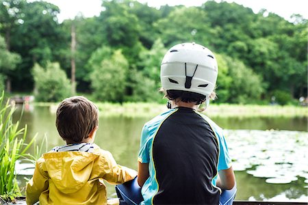 simsearch:614-08487786,k - Two young brothers sitting at water's edge, older brother wearing cycling helmet, rear view Stock Photo - Premium Royalty-Free, Code: 614-09017204