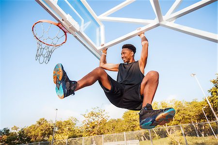 Young man on basketball court, swinging on basketball net frame, low angle view Stock Photo - Premium Royalty-Free, Code: 614-09017228