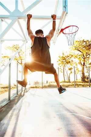Young man on basketball court, swinging on basketball net frame, rear view Stock Photo - Premium Royalty-Free, Code: 614-09017230