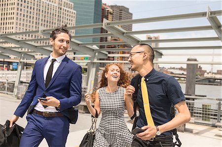 Businessmen and woman with luggage walking and talking on waterfront, New York, USA Stock Photo - Premium Royalty-Free, Code: 614-09017519