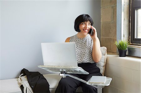 Woman sitting using laptop on laptop stand, speaking on smartphone Stock Photo - Premium Royalty-Free, Code: 614-09017688