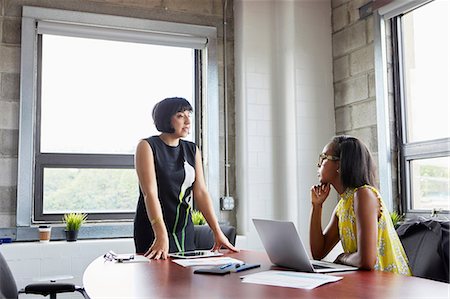 simsearch:614-08926199,k - Woman sitting at desk with laptop, talking to female colleague standing beside desk Stock Photo - Premium Royalty-Free, Code: 614-09017701