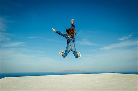 dungaree - Girl in midair, sea and sky in background, O'a, Santorini, Kikladhes, Greece Stock Photo - Premium Royalty-Free, Code: 614-09017789