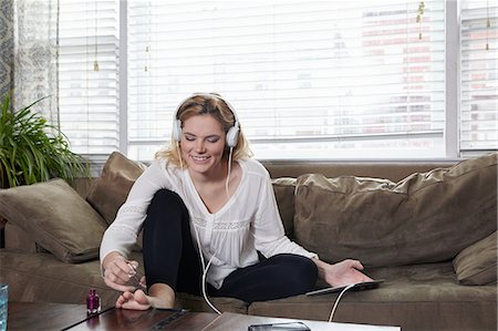 Woman painting nails and listening to music on sofa Stock Photo - Premium Royalty-Free, Code: 614-09017836