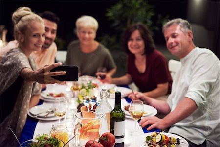 dinner party night - Group of people sitting at table, enjoying meal, young woman taking selfie of group using smartphone Stock Photo - Premium Royalty-Free, Code: 614-09026658