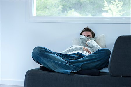 Man reclining on sofa peering from polo neck sweater Stock Photo - Premium Royalty-Free, Code: 614-09026663