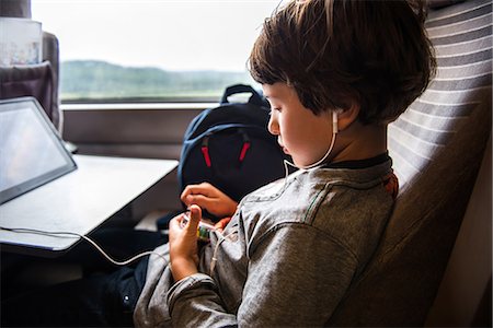 Young boy travelling on train, using digital tablet, wearing earphones Stock Photo - Premium Royalty-Free, Code: 614-09026939