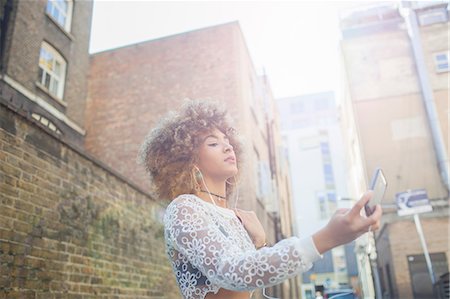 Young woman outdoors, taking selfie, using smartphone, low angle view Photographie de stock - Premium Libres de Droits, Code: 614-09027009