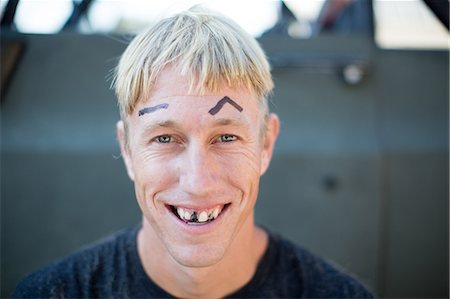 Portrait of young man with badly cut hair, drawn on eyebrows and blacked out teeth Stock Photo - Premium Royalty-Free, Code: 614-09038598